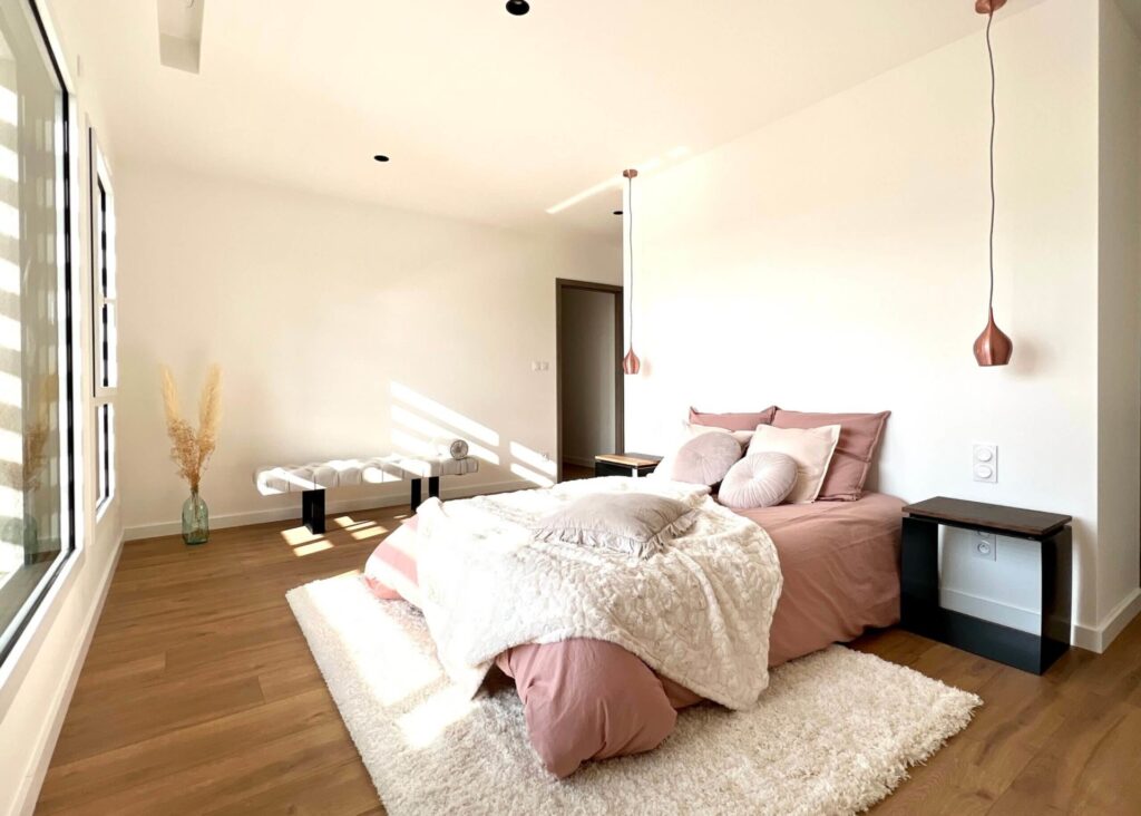 Chambre moderne avec lit, chevet et éclairage suspendu.
